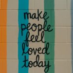 Art graffiti on a cinderblock wall "Make people feel loved today"